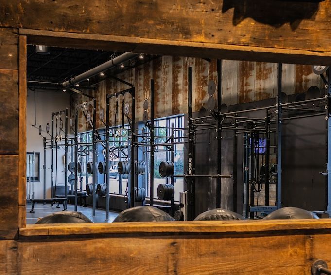 View through wooden frame of a gym with weightlifting racks, equipment, and rustic walls.