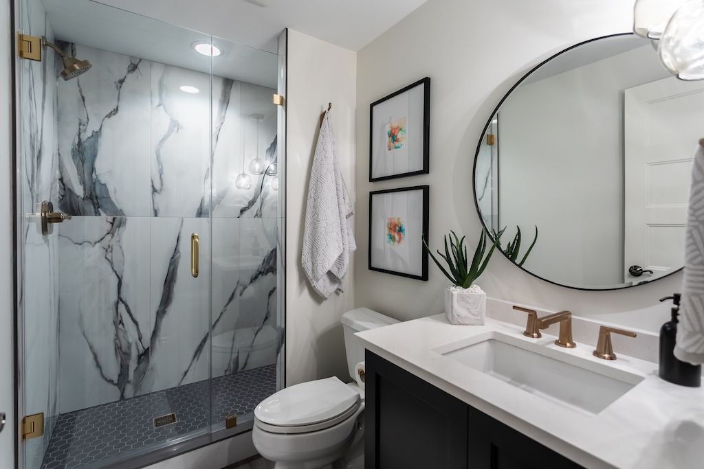 Modern bathroom with marble shower, gold fixtures, and black vanity.