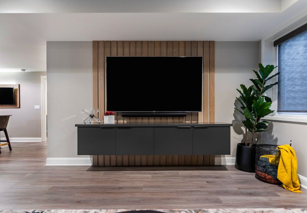 A modern living room with a mounted TV, wood panel accent wall, and floating black cabinet.