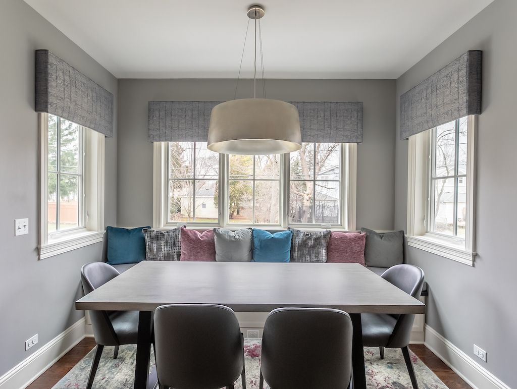Dining room with gray walls, built-in window seat with colorful pillows, rectangular table, and pendant light.