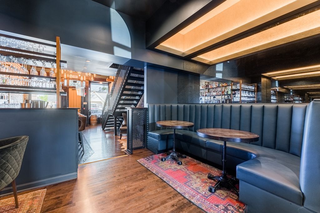 Cozy bar interior with booth seating, small tables, staircase, and a well-stocked bar.