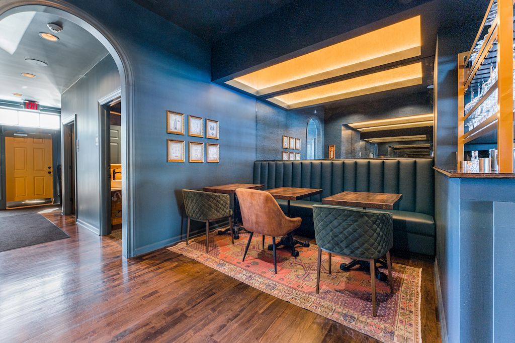 Interior of a restaurant with blue walls, booth seating, and a small rug.