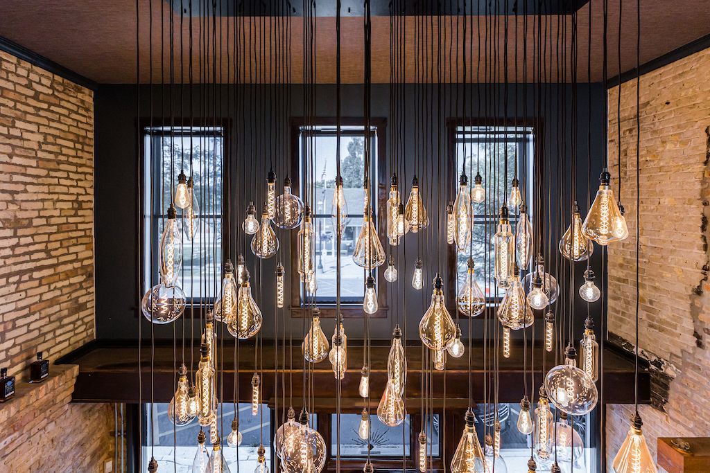 Glass pendant lights suspended in front of windows with exterior view. Brick and dark walls.