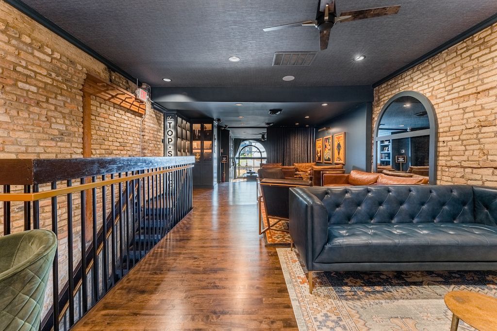 Long, modern interior with exposed brick walls, dark ceiling, couches, and arched doorways.