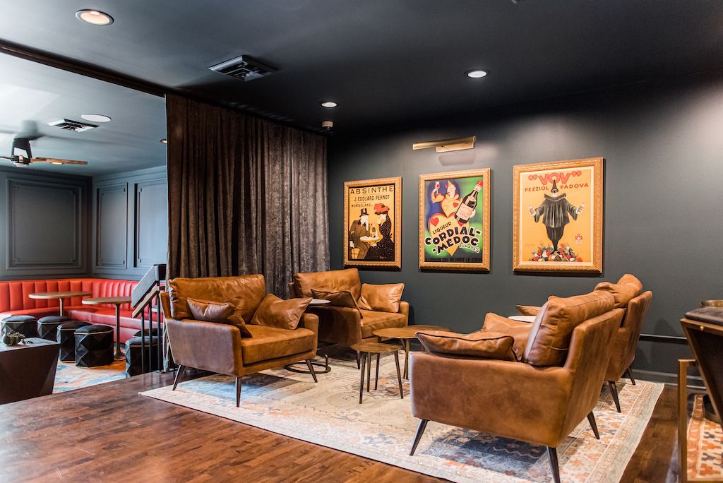 Cozy lounge with leather seating, vintage art, dark walls, and a rug on wooden floors.