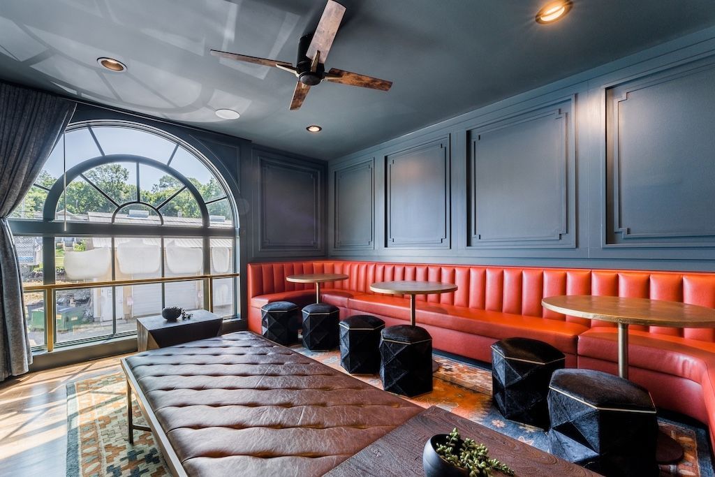 A lounge with red booths, black stools, wooden tables, and a large arched window.