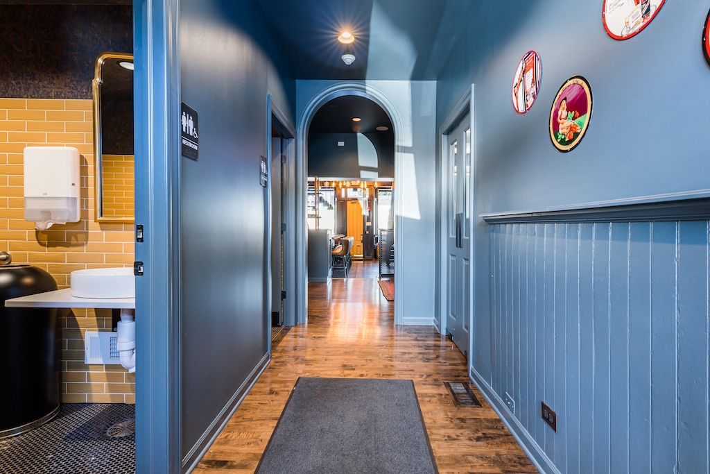 Narrow hallway with blue walls, wood floor, arched doorway, and decorative wall art.