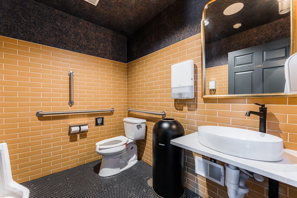 Accessible restroom with gold tile walls, a toilet, sink, and safety bars.
