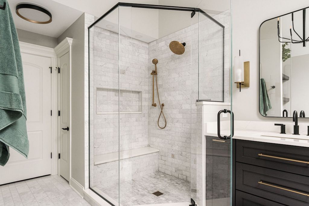 Modern bathroom with a glass shower, marble walls, and gold fixtures.