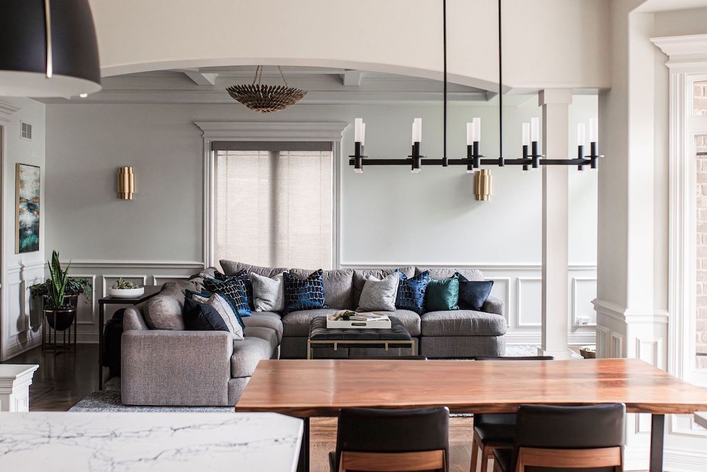 Living room with gray sectional, blue pillows, wood dining table, and modern chandelier.