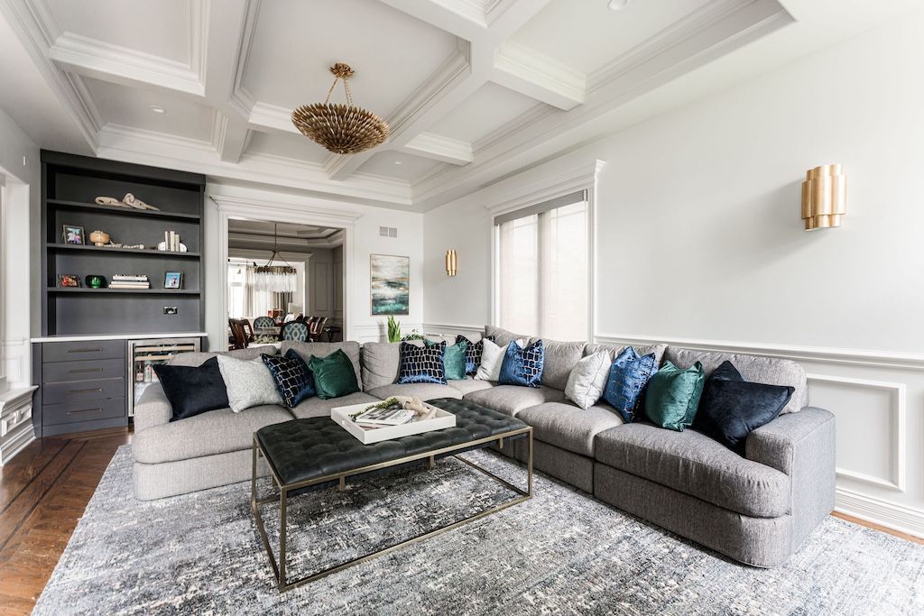 Spacious living room with gray sectional sofa, patterned rug, white walls, and decorative ceiling beams.