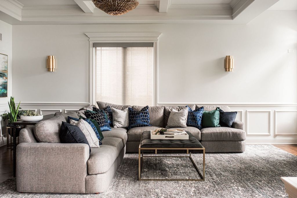 Cozy living room with a gray sectional sofa, gold sconces, and a gray patterned rug.