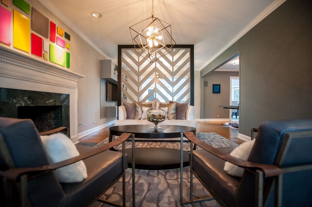 Living room with modern decor; gray walls, colorful art, fireplace, patterned screen, leather chairs.