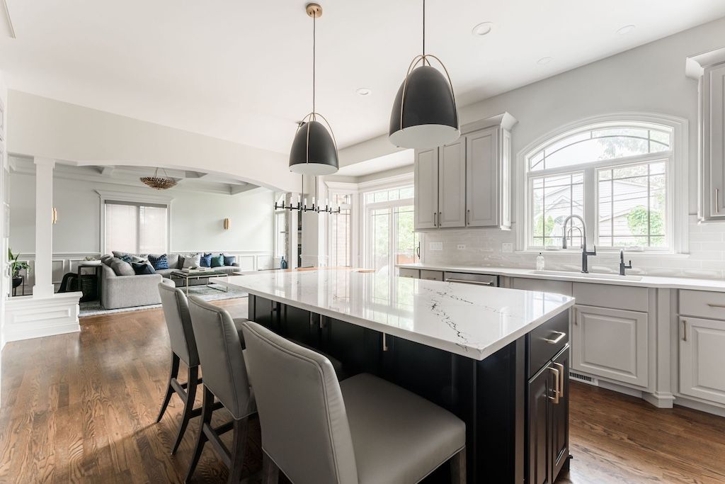 Spacious modern kitchen with island, pendant lights, seating, and view of a living area.