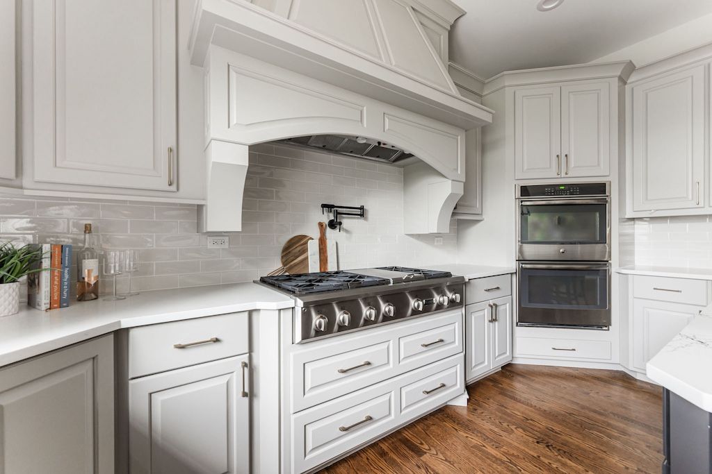 Bright white kitchen with a large range and hood, wooden floors, and white cabinets.