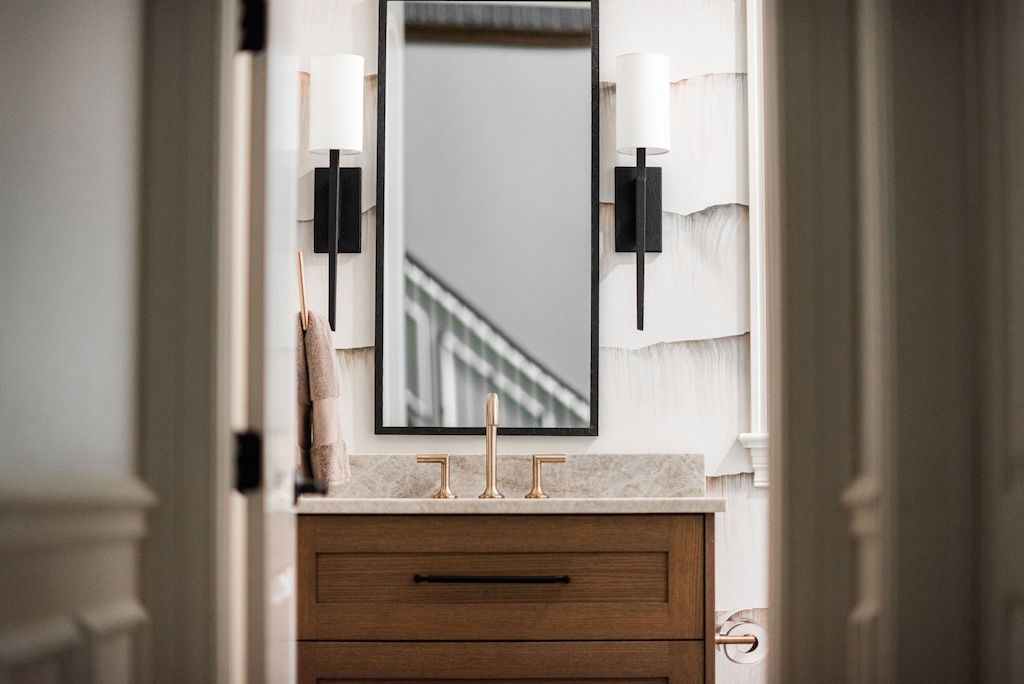 Bathroom vanity with mirror, sconces, and wood cabinet, viewed through an open doorway.