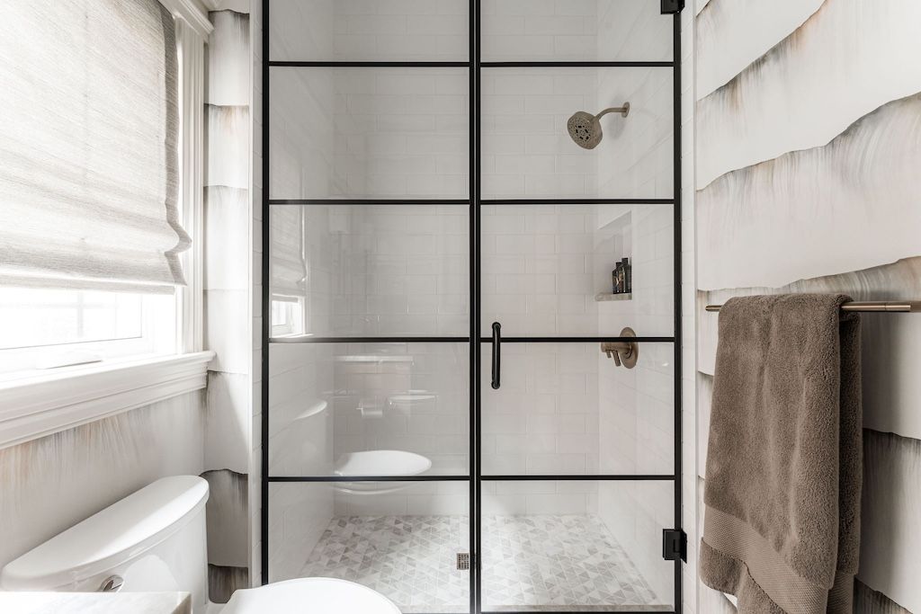 Bathroom with a black-framed glass shower door. White toilet, window with blind, and towel rack on the right.