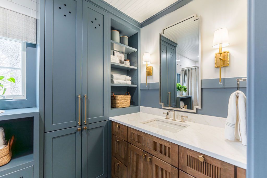 Blue and wood-toned bathroom with cabinets, a countertop with sink, mirror, and sconces.