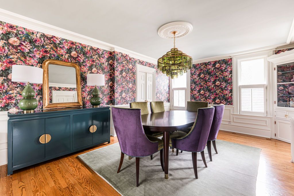 Dining room with floral wallpaper, purple chairs, teal sideboard, and green chandelier.