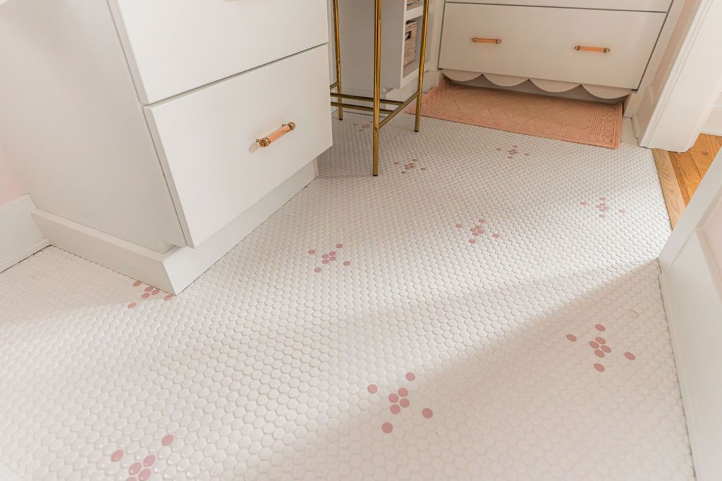 White and pink penny tile bathroom floor, with white cabinets and gold accents.