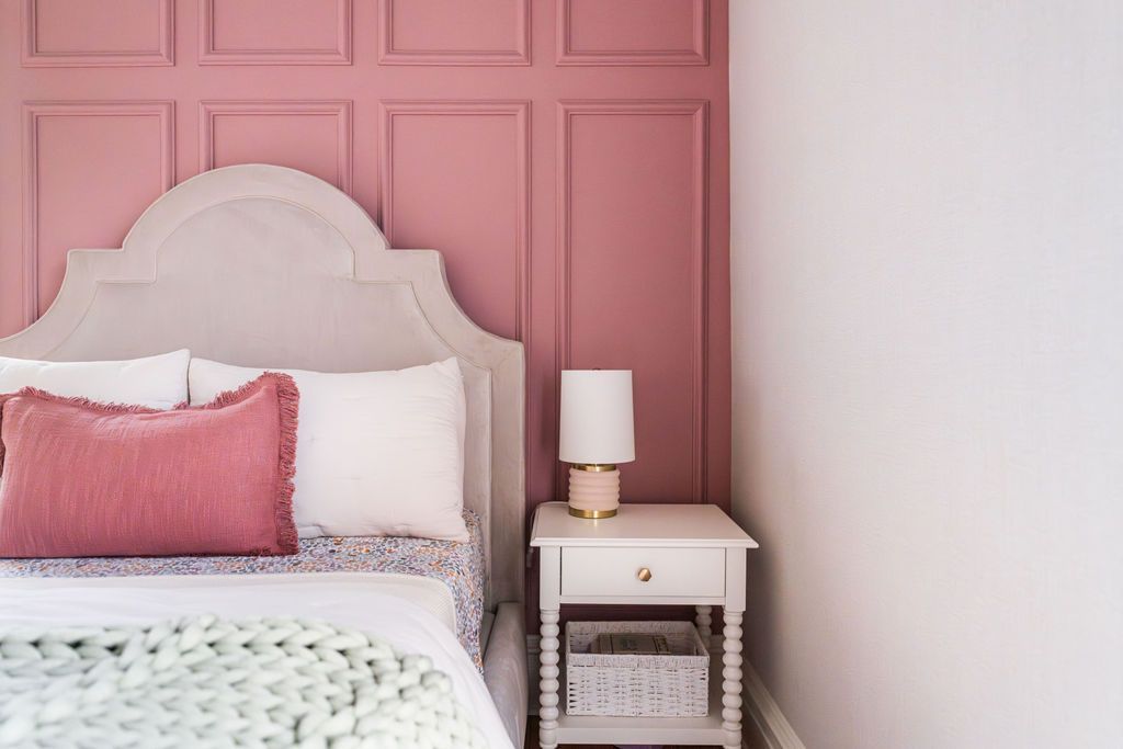 Bedroom with pink paneled wall, upholstered headboard, and white nightstand.