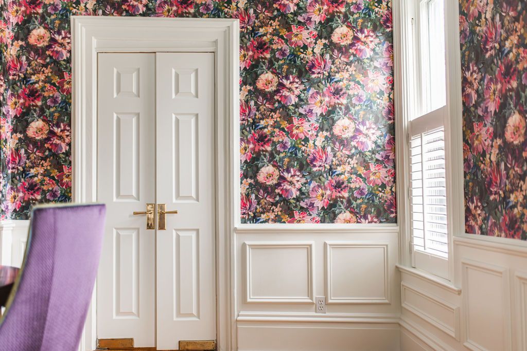 Floral wallpapered room with white trim, double doors, and a window. A purple chair is partially visible.