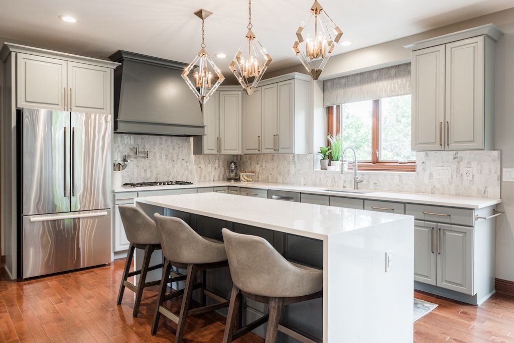Modern kitchen with gray cabinets, white countertops, island with bar stools, and chandeliers.