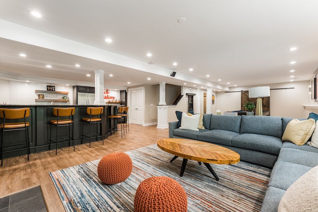 Spacious finished basement with blue sectional sofa, wooden coffee table, and bar with stools.