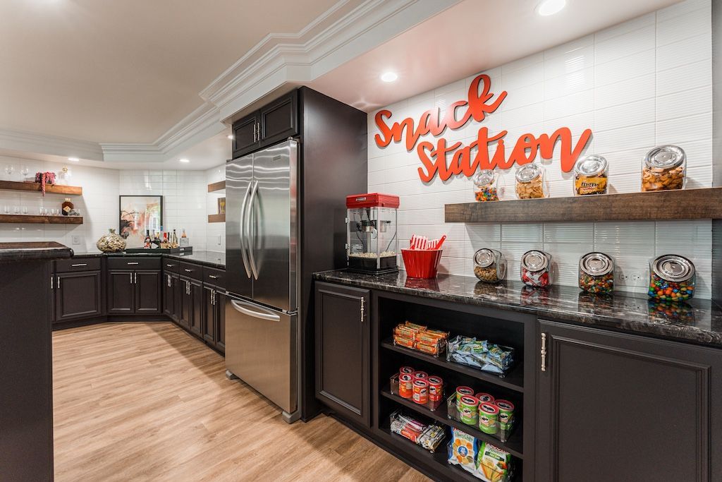 Snack station in a room with dark cabinets, stainless steel fridge, and wooden shelves. 