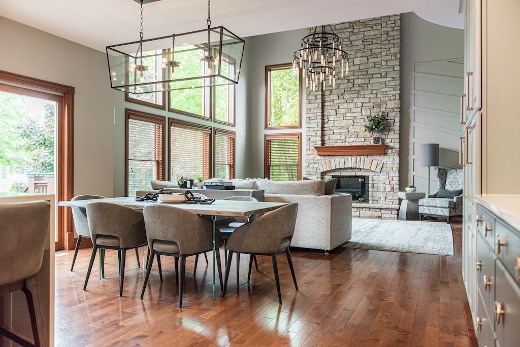 A modern dining and living room with a large table, sofa, fireplace, and hardwood floors.