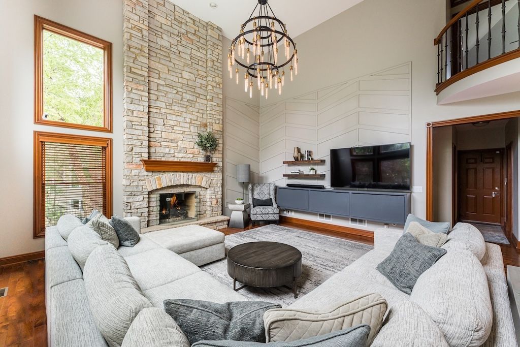 Living room with stone fireplace, large sectional sofa, chandelier, and a TV on a gray wall.