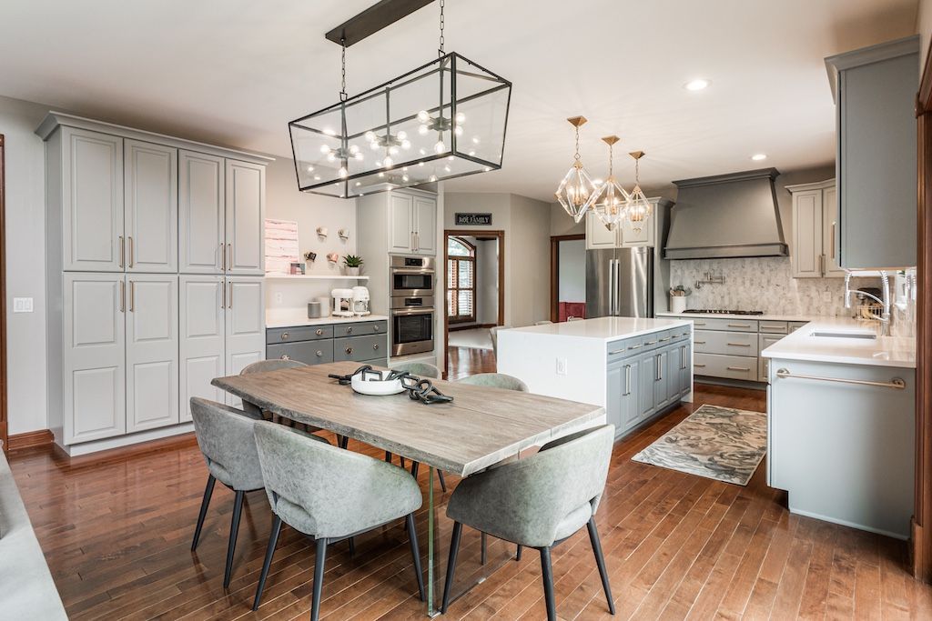 Spacious modern kitchen with gray cabinets, large island, dining table, pendant lights, and hardwood floors.