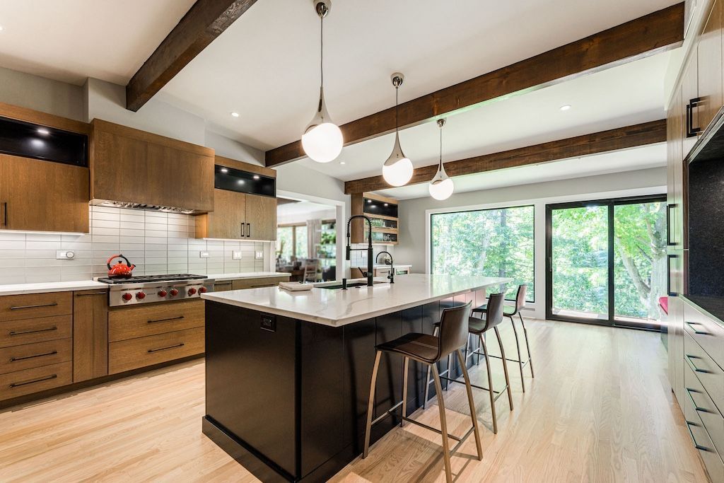 Modern kitchen with wood cabinets, black island, light wood floor, and large windows.