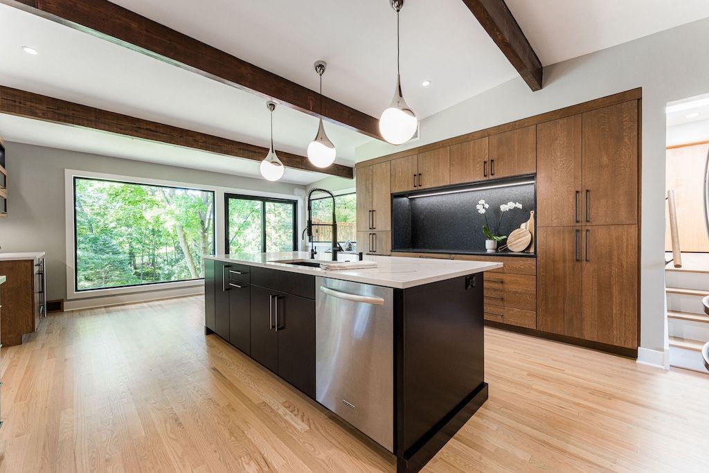 Modern kitchen with island, stainless steel appliances, wood cabinets, and large windows.