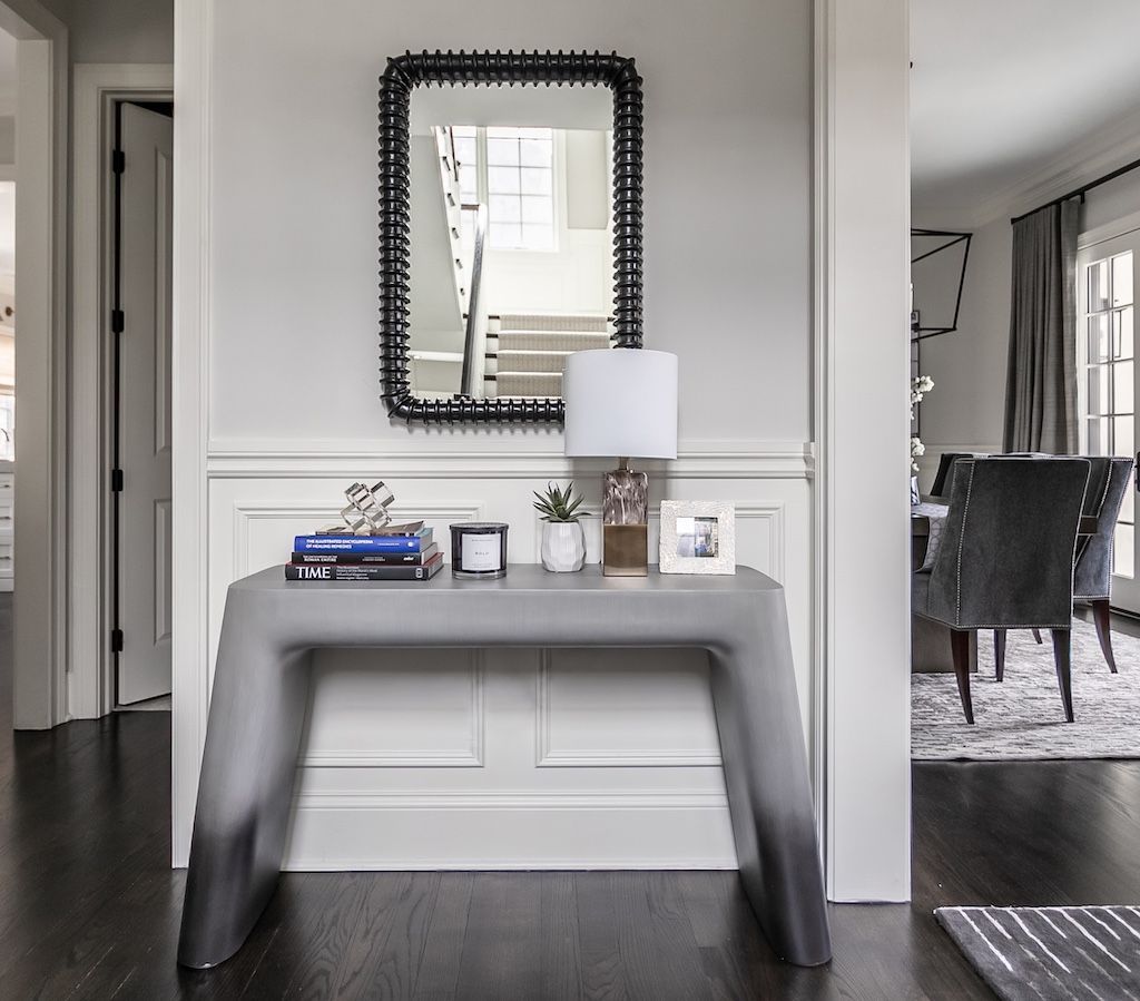 A gray console table with decor, a mirror, and a lamp in a modern hallway.