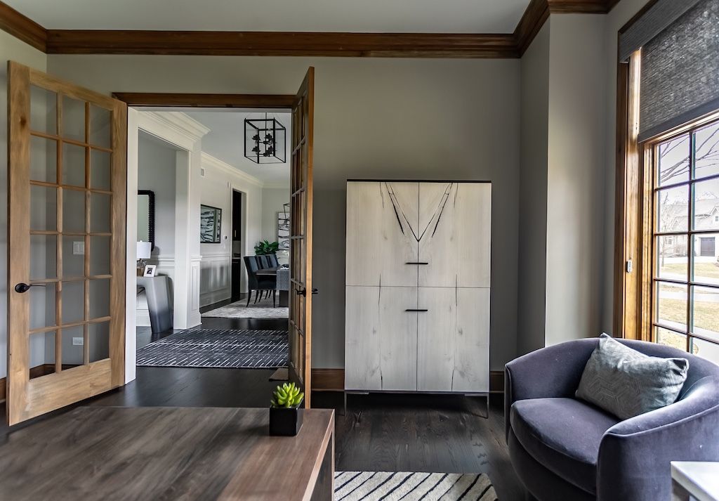 A room with a wooden cabinet, blue armchair, and French doors leading to another room.
