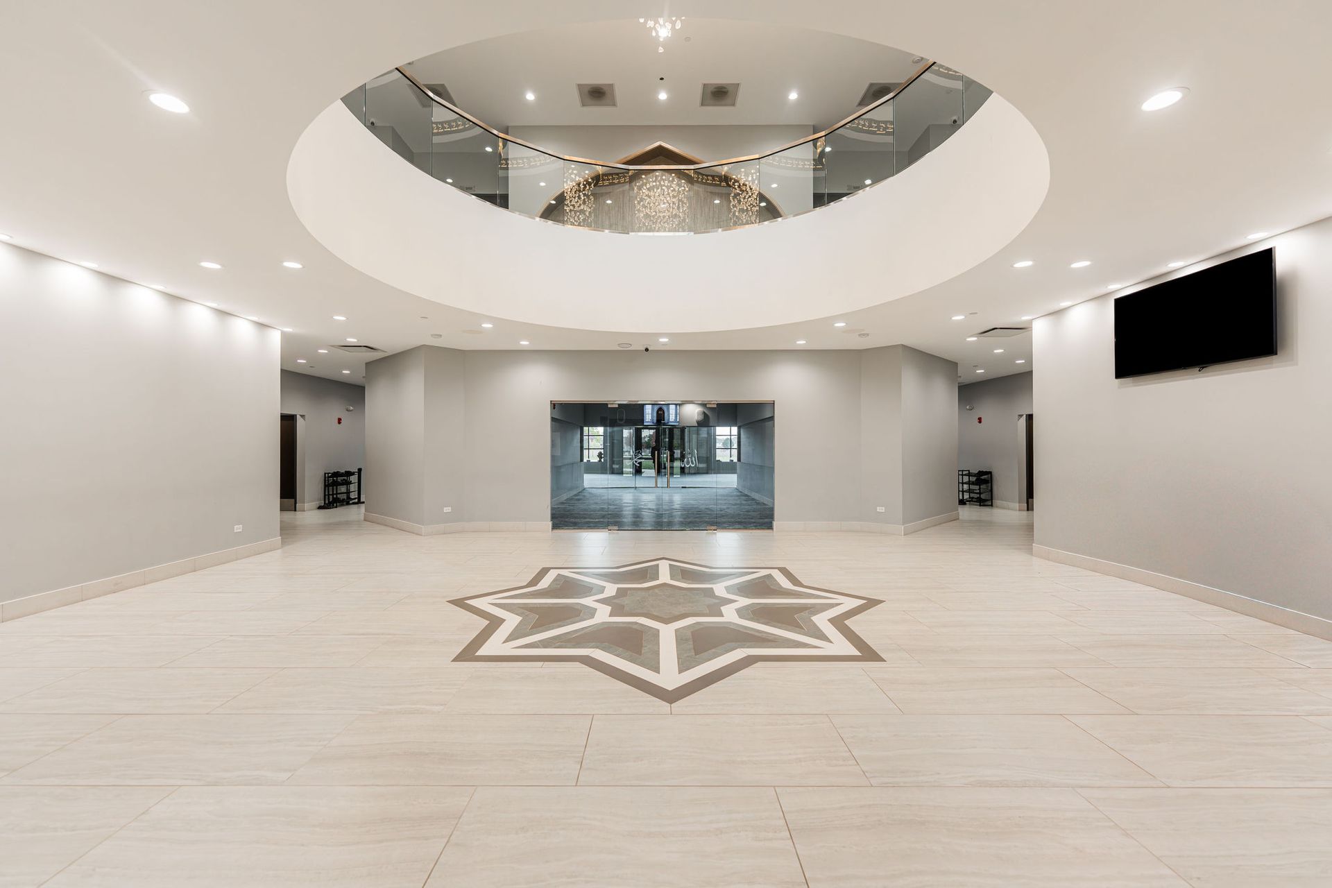 Spacious, modern interior with tiled floor and starburst design. Glass doors lead to another area. Overhead circular balcony.