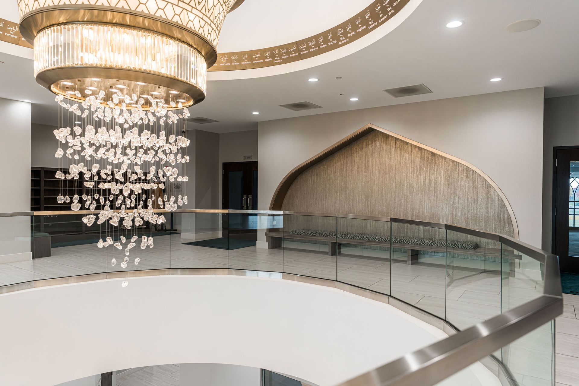Grand, light-filled foyer with a large chandelier and a curved glass railing.