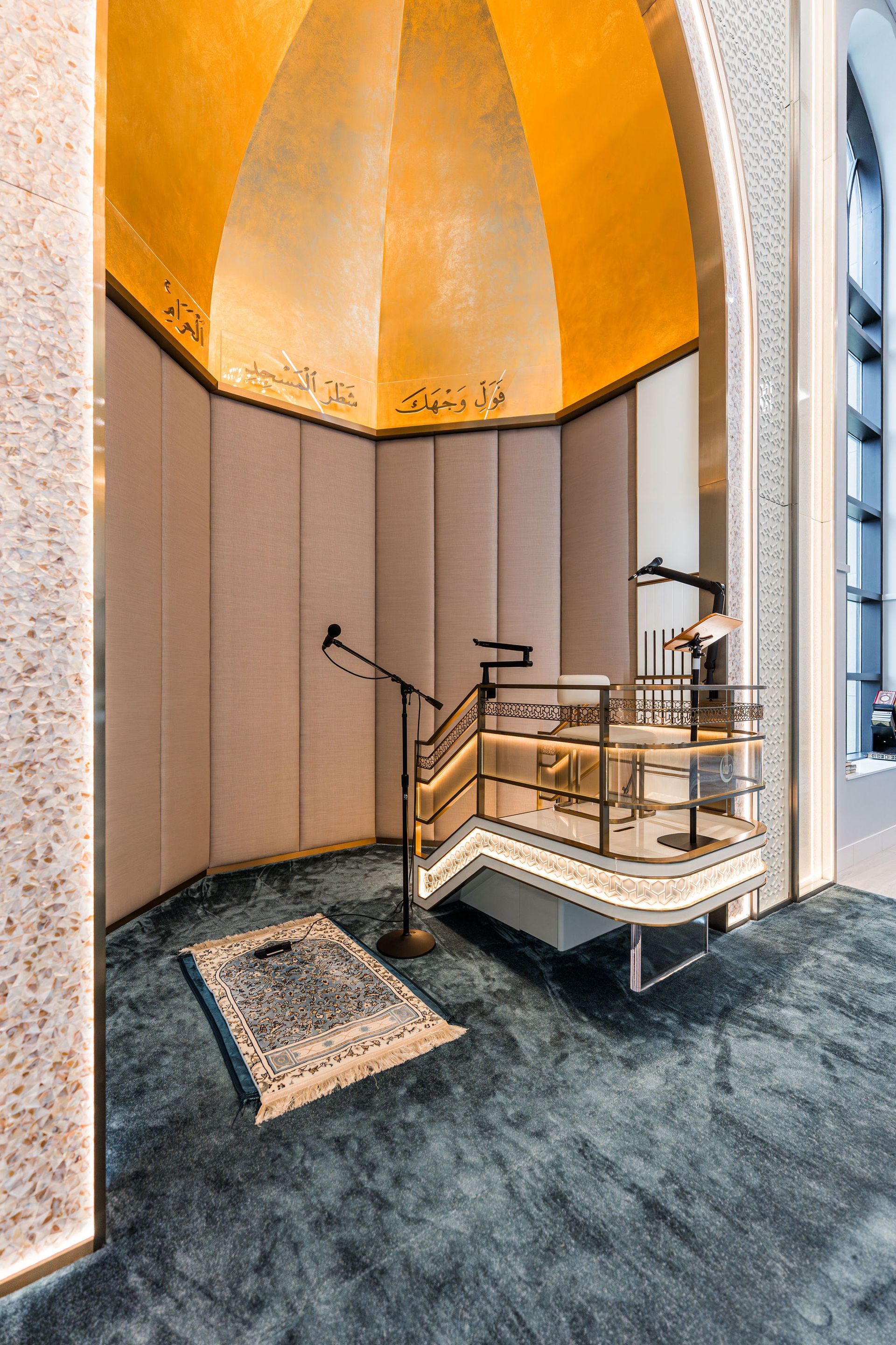 Prayer room with a golden dome and a small elevated platform. A prayer rug lies on a teal carpet.