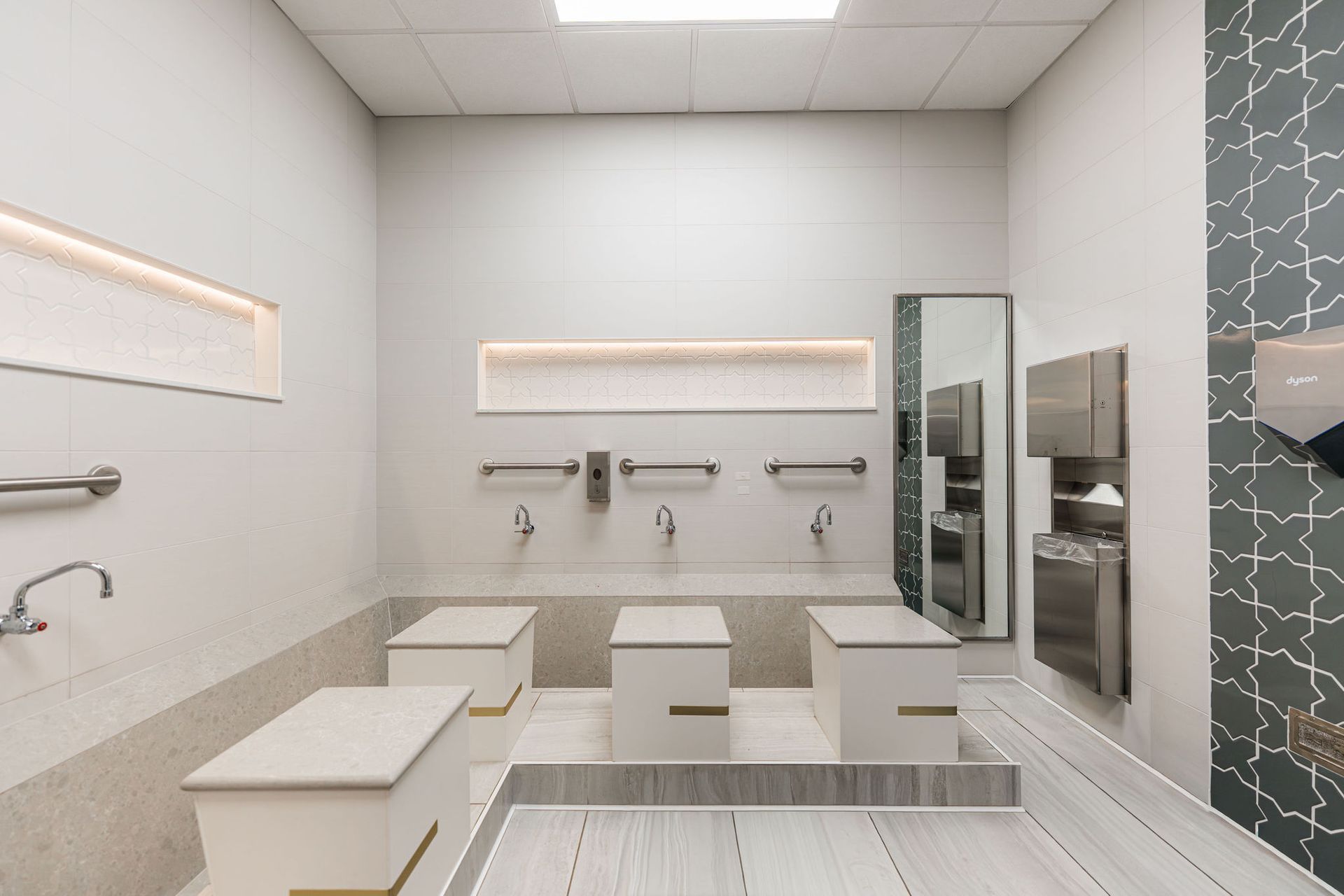 Modern public restroom with white sinks, stainless steel fixtures, and decorative accent wall.