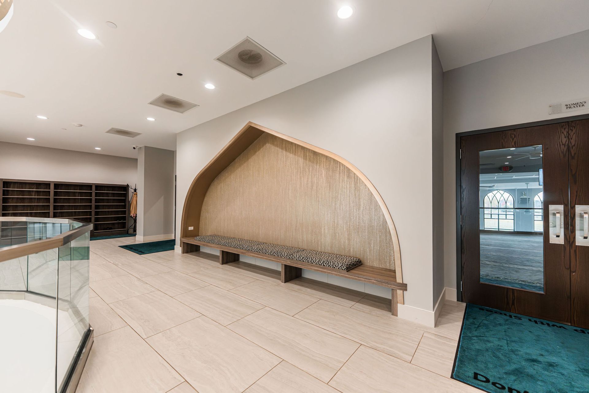 Hallway with built-in bench, wooden arch design, light-colored tile floor, and a door on the right.