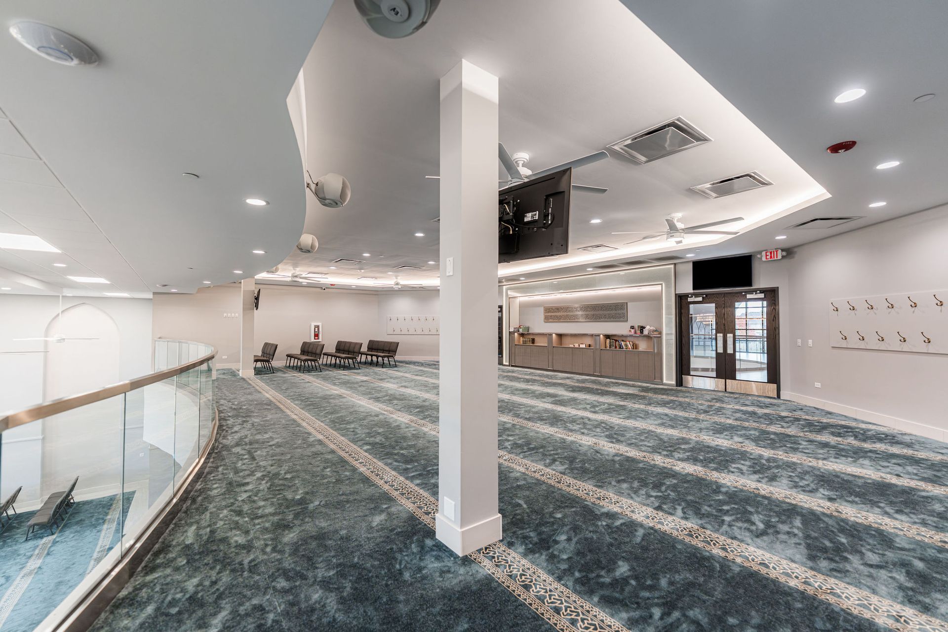 Interior of a mosque with blue patterned carpet, white walls, and a balcony.