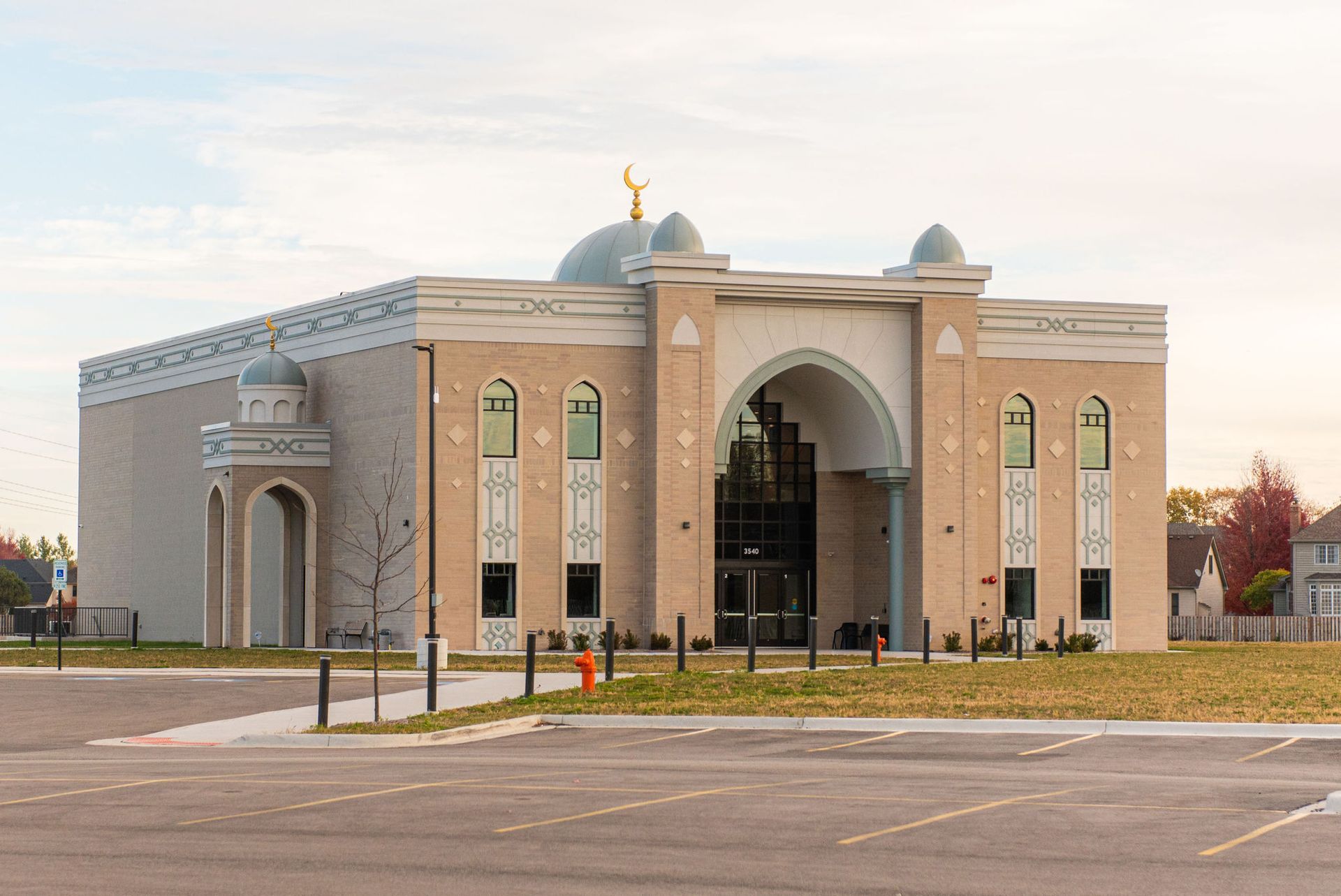 Mosque with tan brick facade, blue dome, and gold crescent, set against a cloudy sky.