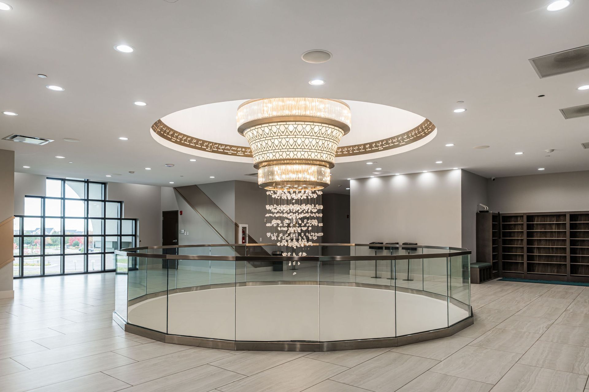 Spacious, modern lobby with large chandelier, circular railing, and built-in shelving.