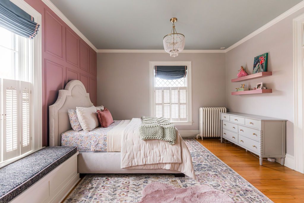 Bedroom with pink accent wall, upholstered bed, patterned rug, and decorative shelves.
