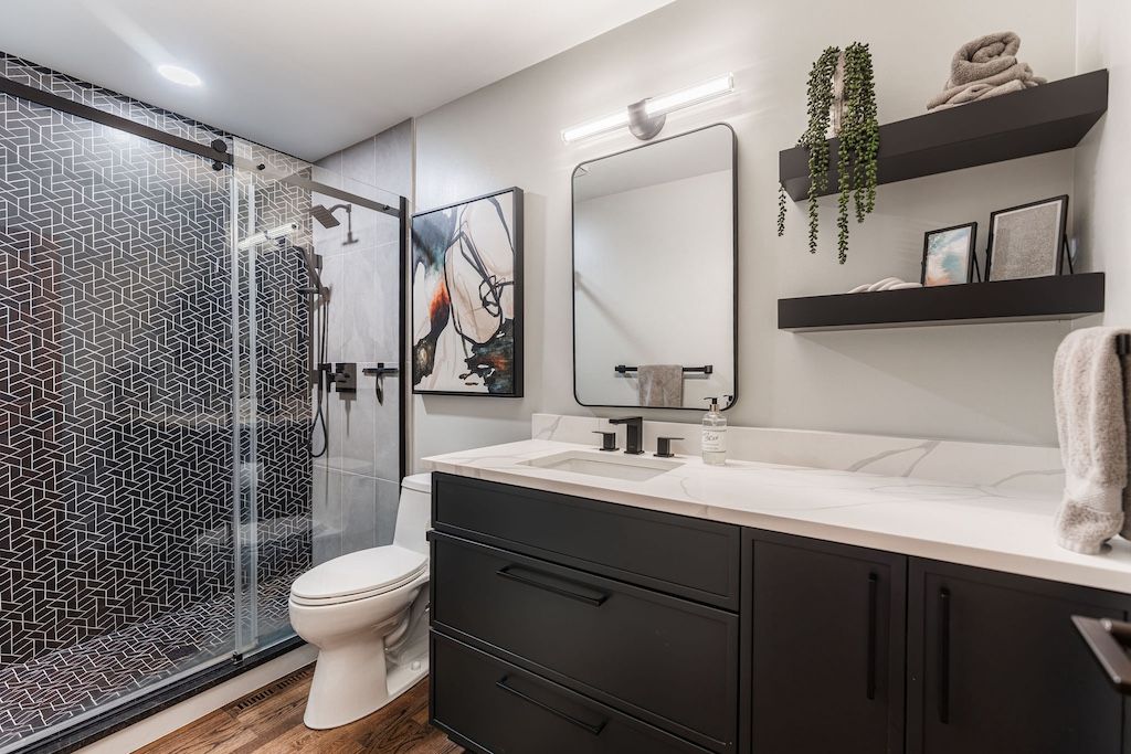 Modern bathroom with black vanity, textured shower door, and floating shelves with decor.