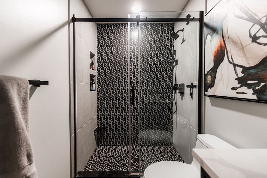 Bathroom with black shower enclosure, black and white tile, white walls, and a towel on a rack.
