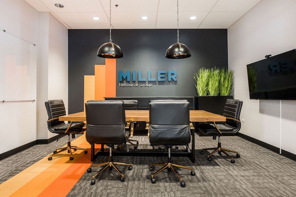 Conference room with wood table, black chairs, and dark accent wall with company logo.
