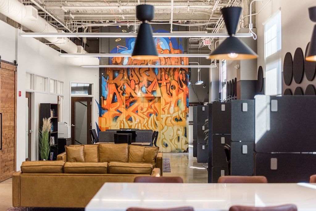 Spacious modern office with graffiti art, brown leather sofa, black pendant lights, and large gray storage units.