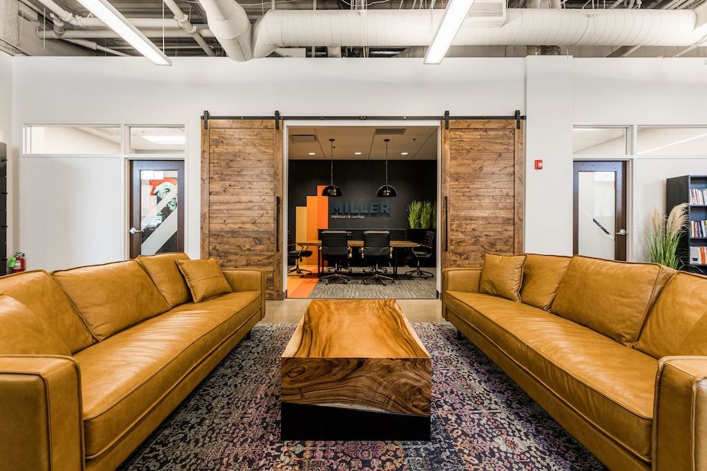 Lounge area with two brown leather sofas facing a wooden coffee table and sliding barn doors.